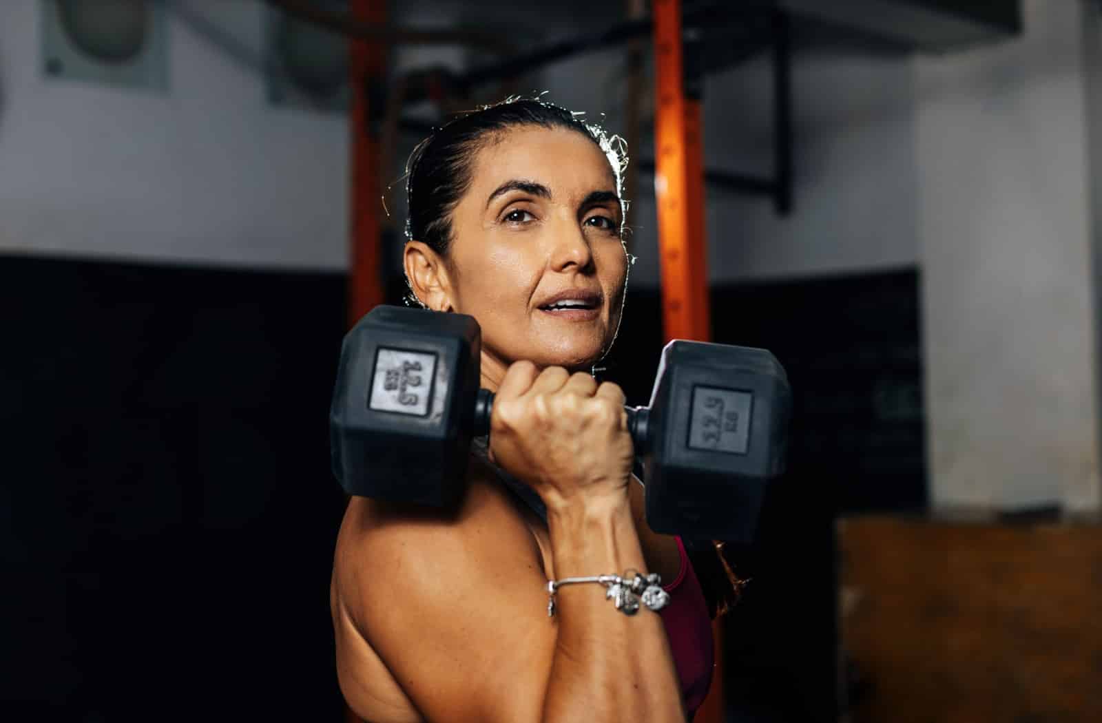 A woman holding a dumbbell at her shoulder during a strength training session.