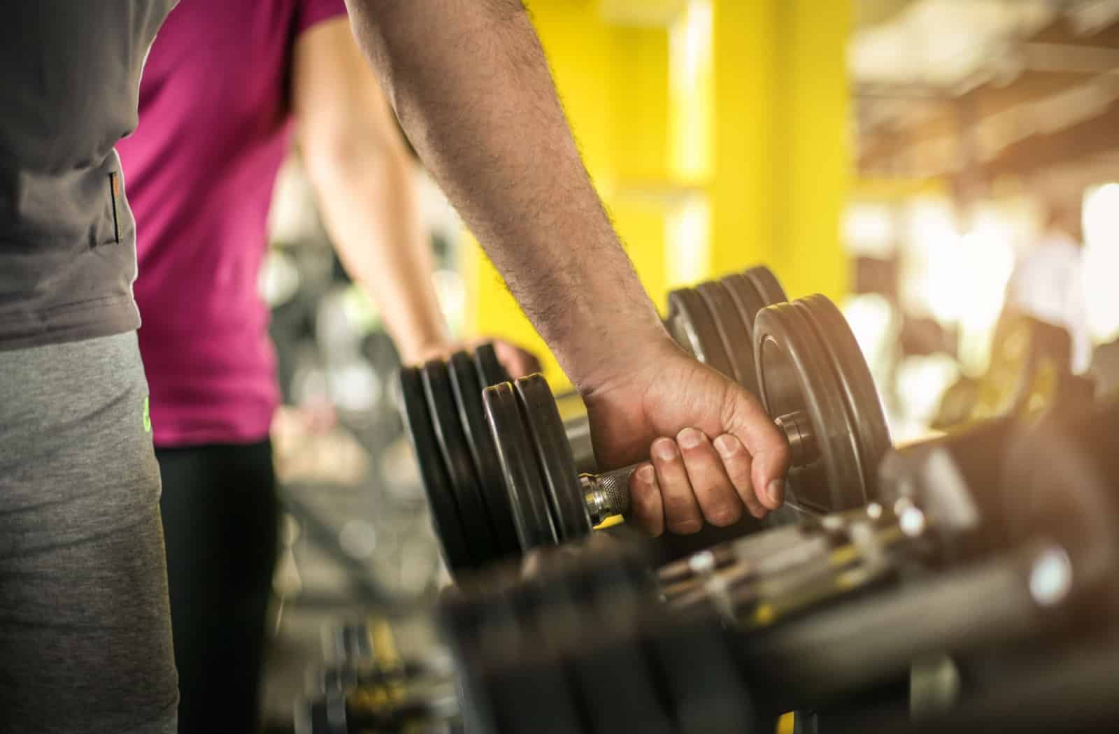 A hand grabbing a free weight from a weight rack at the gym.